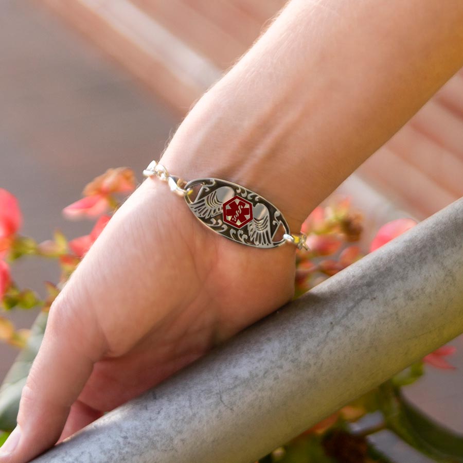 Woman wearing Guardian Angel Medical ID Tag on an LH bracelet. Stainless ID tag has angel wings, antique finish, red caduceus