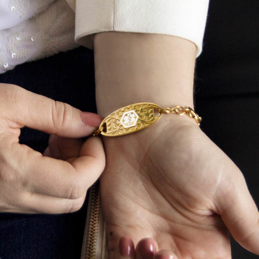 Woman wearing Gold Tone Gardenia Medical ID Tag with inlaid Gardenia pattern and white caduceus. Worn on beaded bracelet