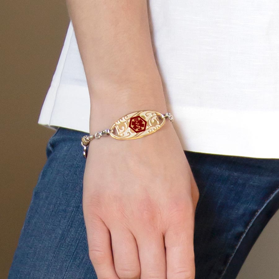 Woman wearing Golden Filigree Medical ID Tag on LH bracelet. Gold tone plated stainless tag, filigree pattern, red caduceus