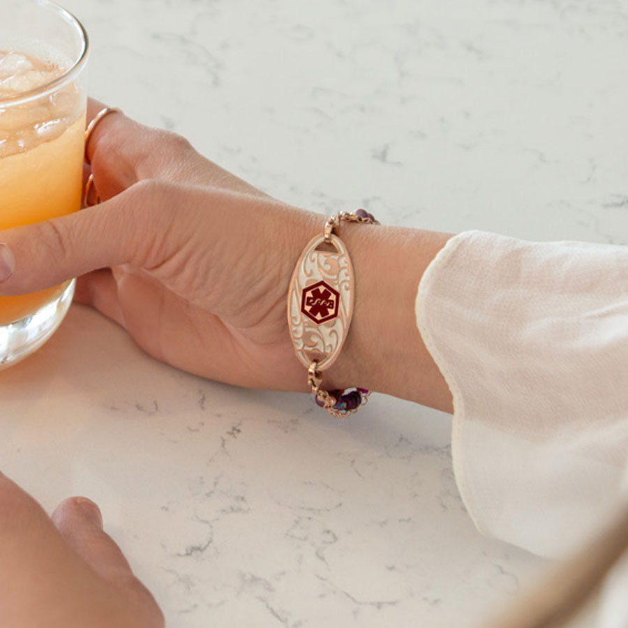 Woman wearing the scroll design Rose Gold Tone Filigree Medical ID Tag with red caduceus on a Lauren’s Hope med ID bracelet