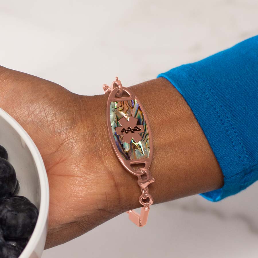 Woman holding bowl of blueberries wearing rose gold tone stainless steel flat medical ID tag with natural abalone inlay and rose gold tone medical symbol.