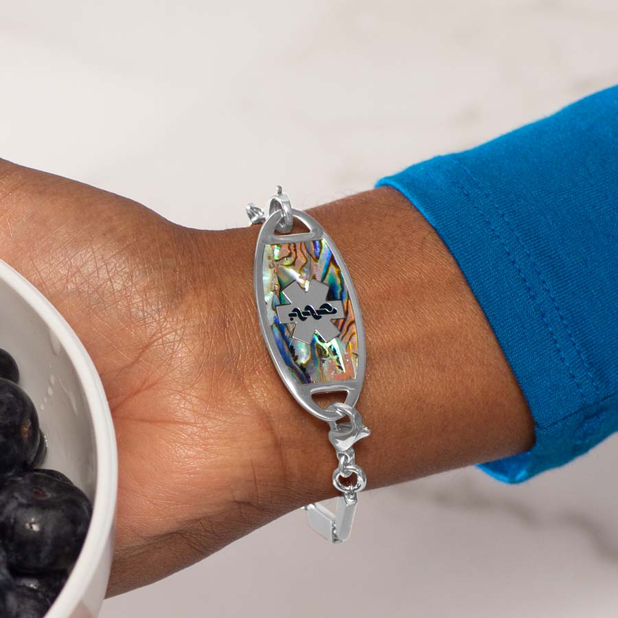 Woman hold bowl of blueberries wearing flat stainless steel med ID tag with natural abalone inlay and silver tone medical symbol.