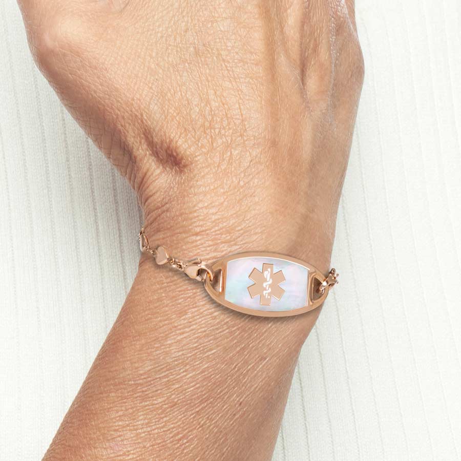 Woman in cream sweater wearing rose gold medical ID tag with mother of pearl inlay and rose gold medical caduceus symbol