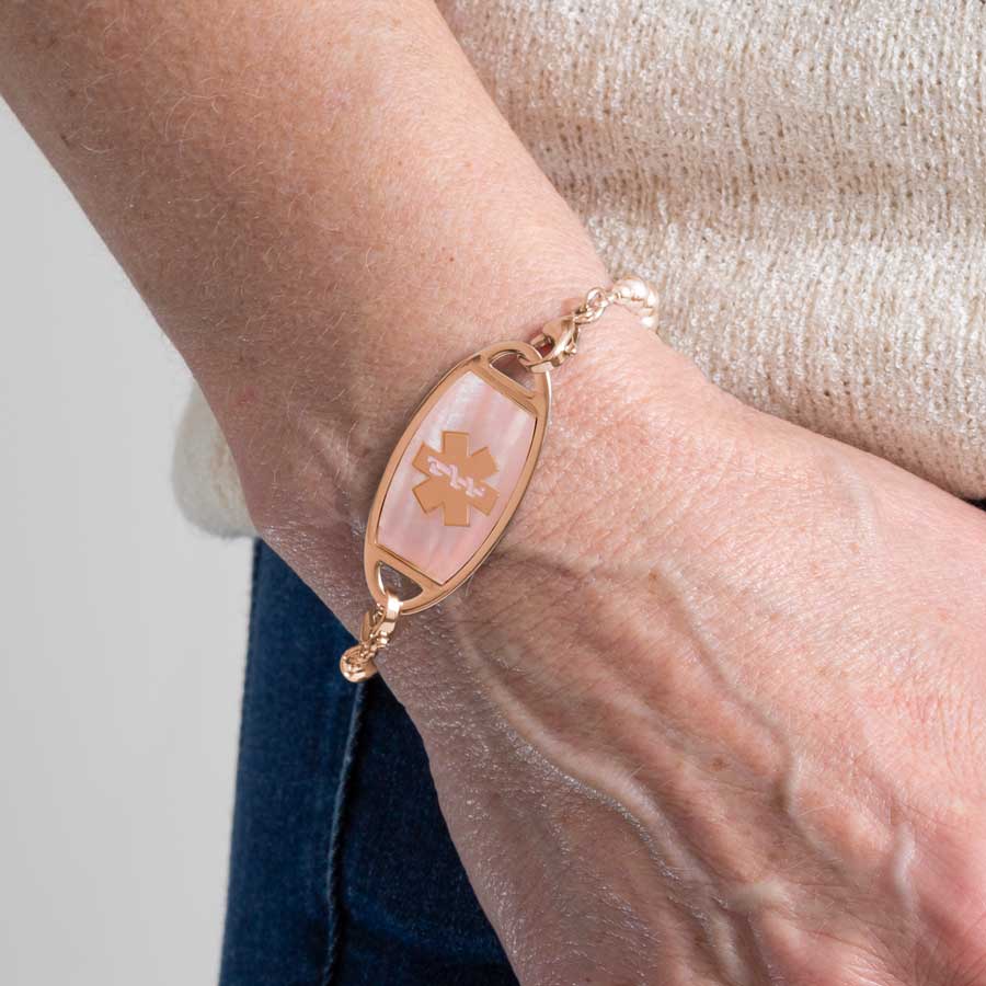 Rose gold and pink mother of pearl medical ID bracelet worn by woman with white shirt and rose gold bracelet