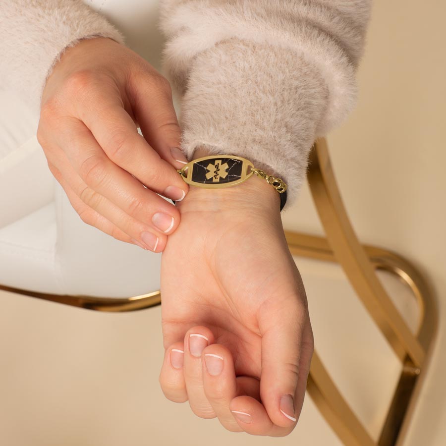 Woman wearing gold tone stainless steel medical ID tag with black marble inlay and gold tone medical symbol at the center.