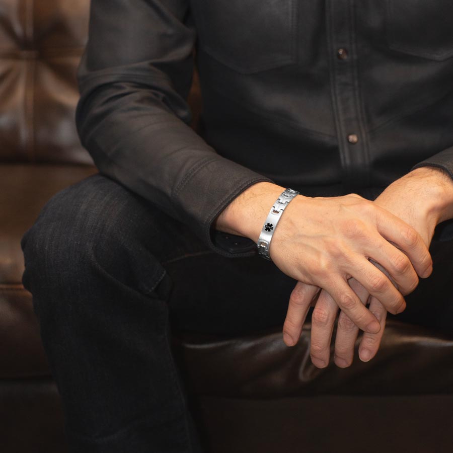 Man wearing stainless steel link style medical alert bracelet with black medical symbol at the center.