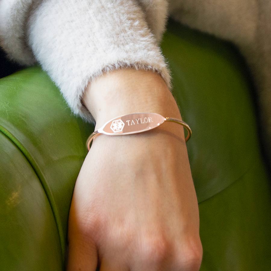 Woman wearing delicate rose gold medical ID cuff bracelet with custom engraving