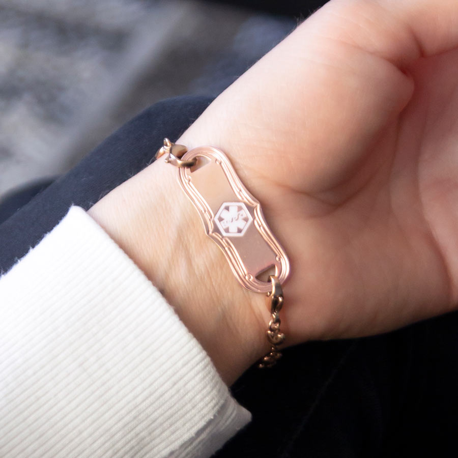 Woman showing rose gold medical alert tag with decorative edge and white medical caduceus