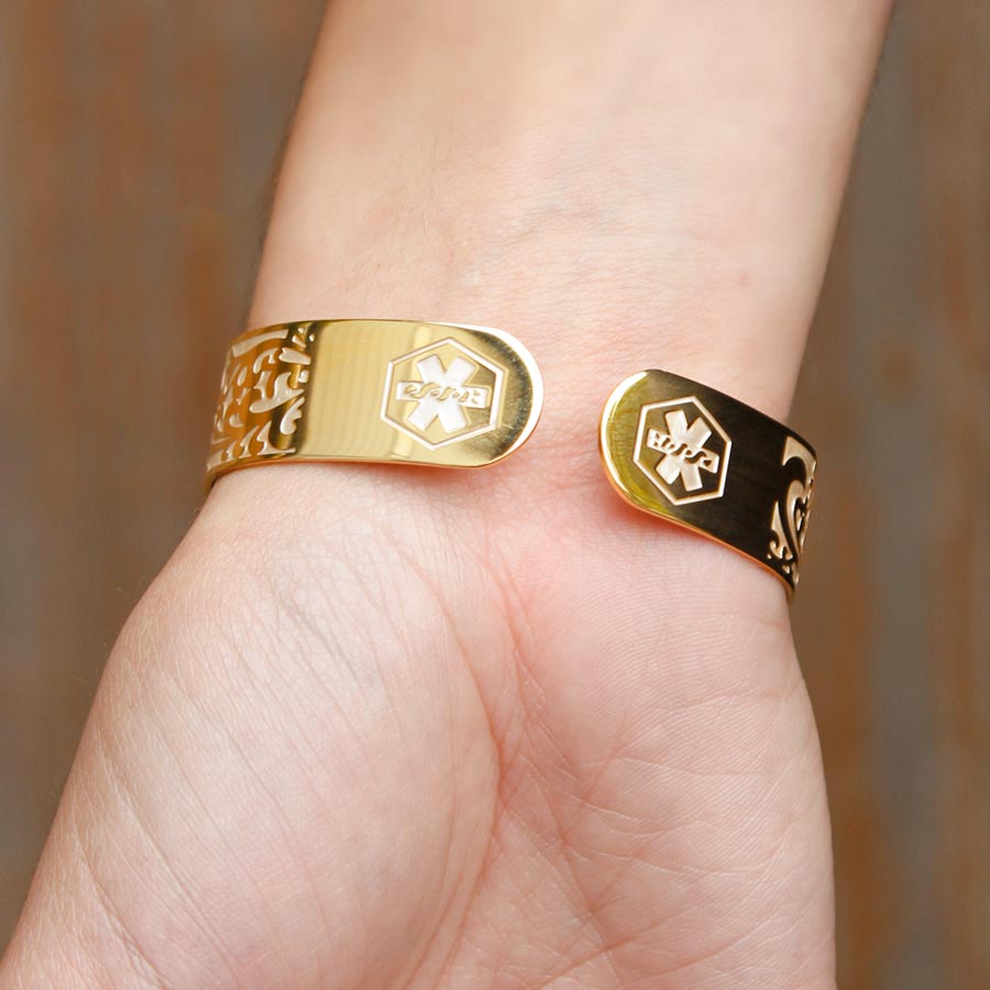 Woman wearing Golden Filigree Medical ID Cuff. Stainless yellow gold tone filigree with pearlescent finish. White caduceus