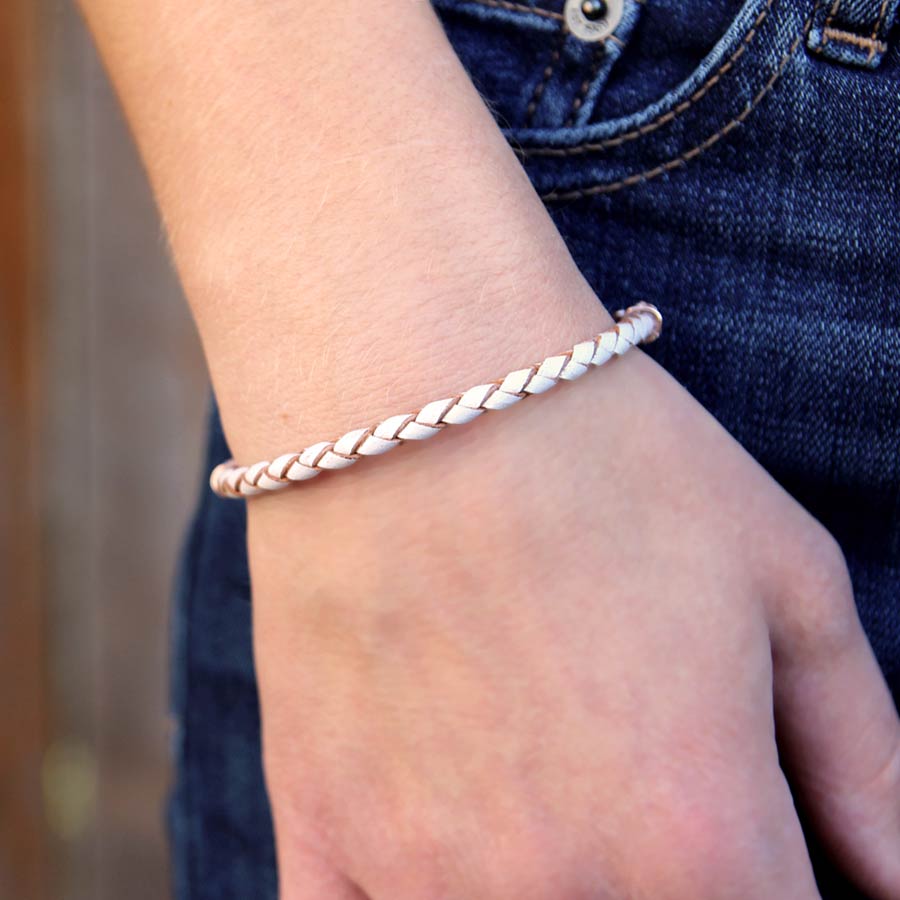 Woman wearing cream and rose gold braided leather bracelet with hands at her side.