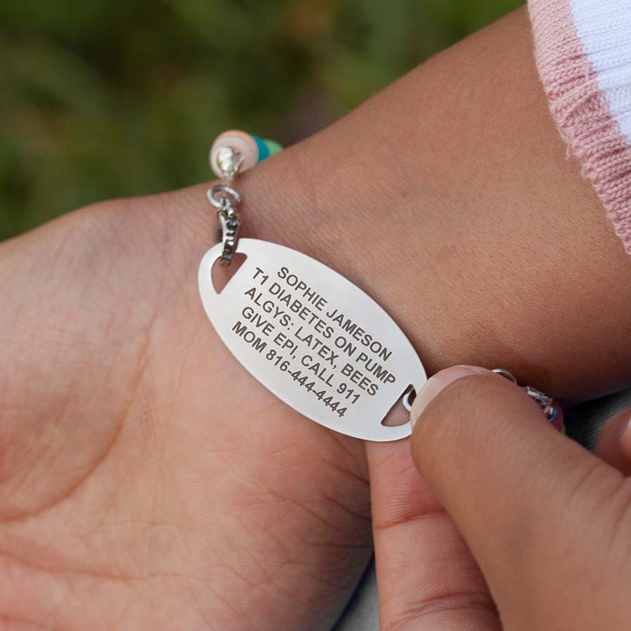 Little girl flipping over her medical ID tag to show medical details custom laser engraved on back of tag.