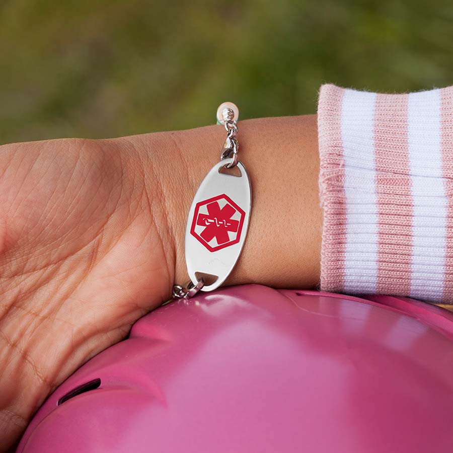 Little girl showing the medical alert tag on colorful medical ID bracelet with red caduceus facing forward.