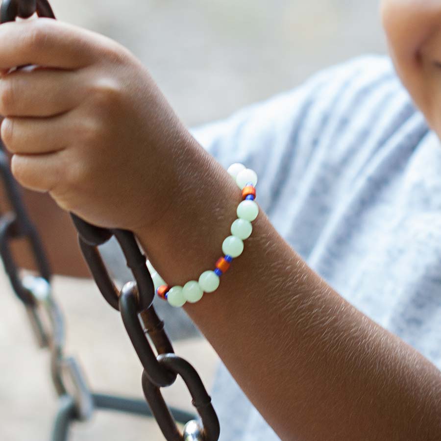 Young boy on swing wearing beaded medical ID bracelet with glow-in-the-dark beads.