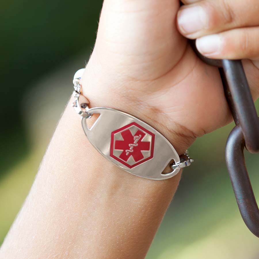 Little boy on swing showing medical alert tag on medical ID bracelet with red caduceus facing forward.