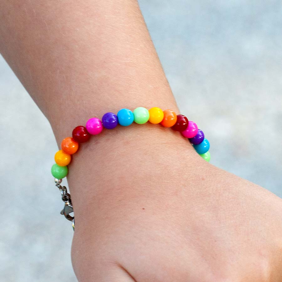 Young girl riding scooter, wearing beaded medical ID bracelet with rainbow colored beads.