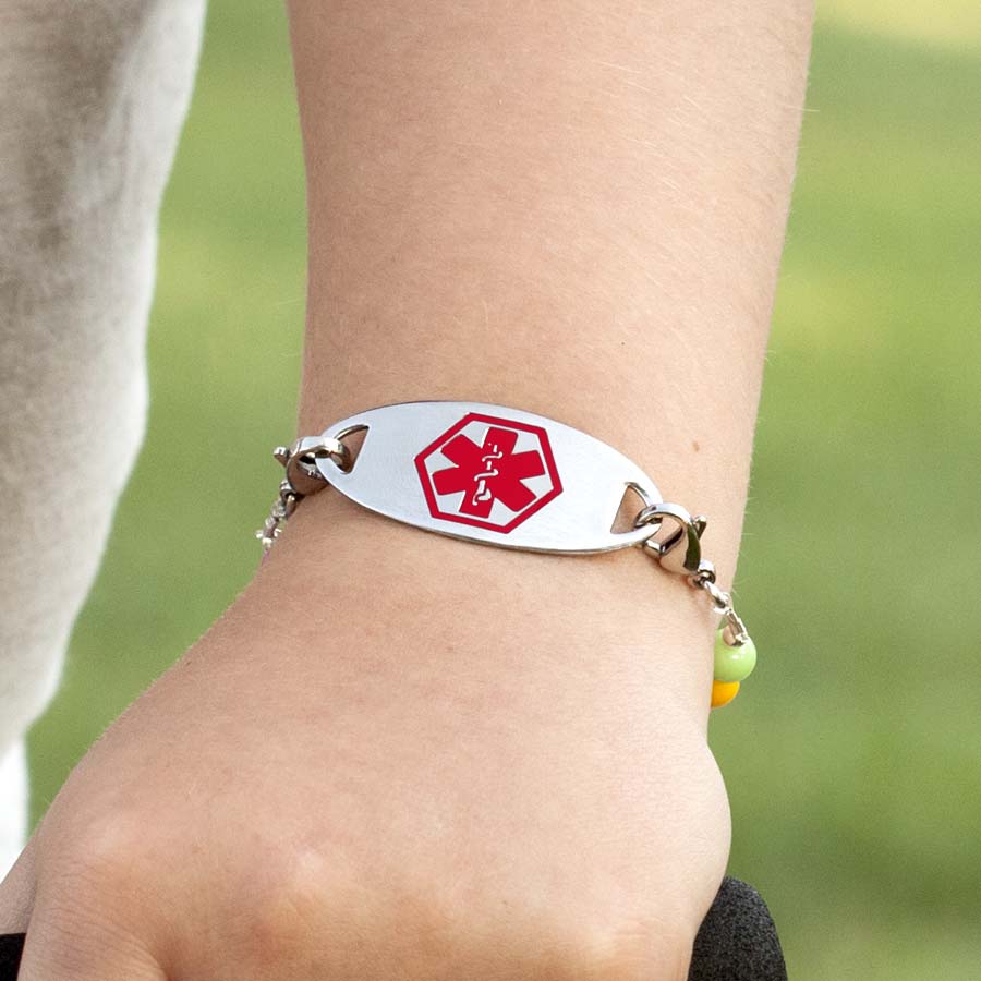 Little girl on scooter, showing medical alert tag on medical ID stretch bracelet with red symbol facing forward.