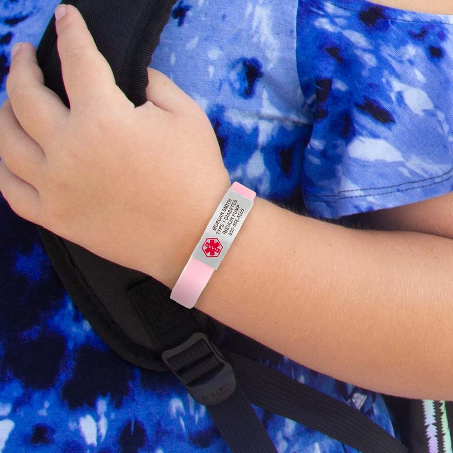 Smiling girl with colorful shirt and backpack, holding backpack strap and wearing soft pink glow-in-the-dark silicone bracelet.