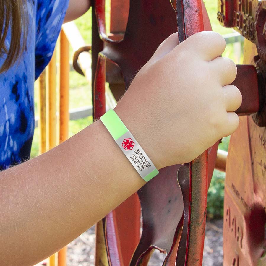 Young girl in colorful shirt playing on train car at the park, wearing green glow-in-the-dark silicone bracelet.