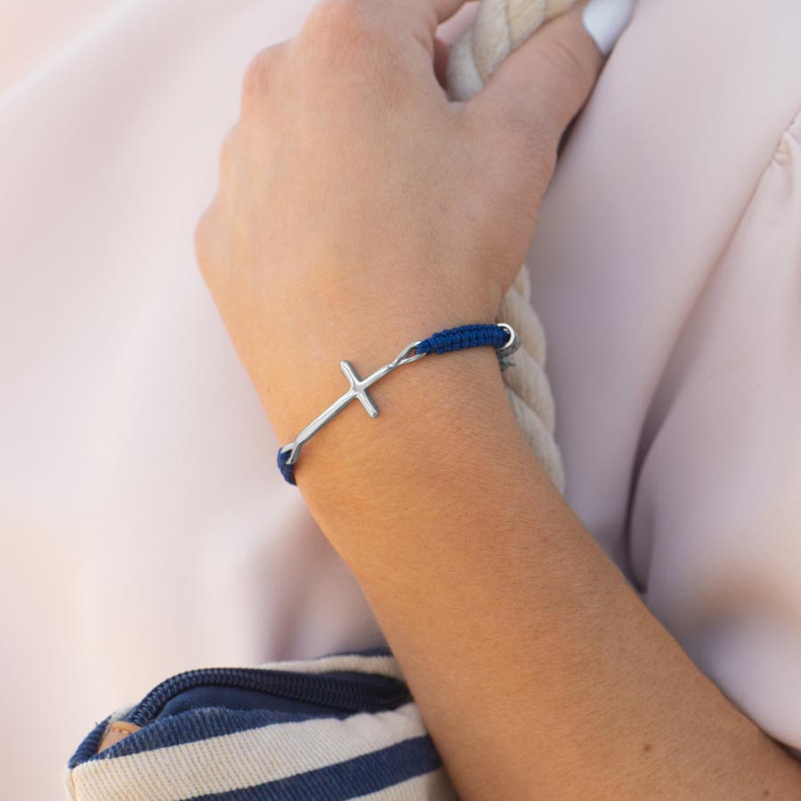 Woman holding bag strap wearing navy blue macrame medical ID bracelet with silver cross center piece.