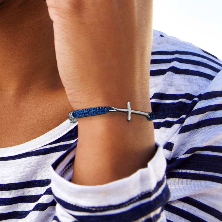 Woman in striped top wearing navy blue macrame medical ID bracelet with silver cross center piece.