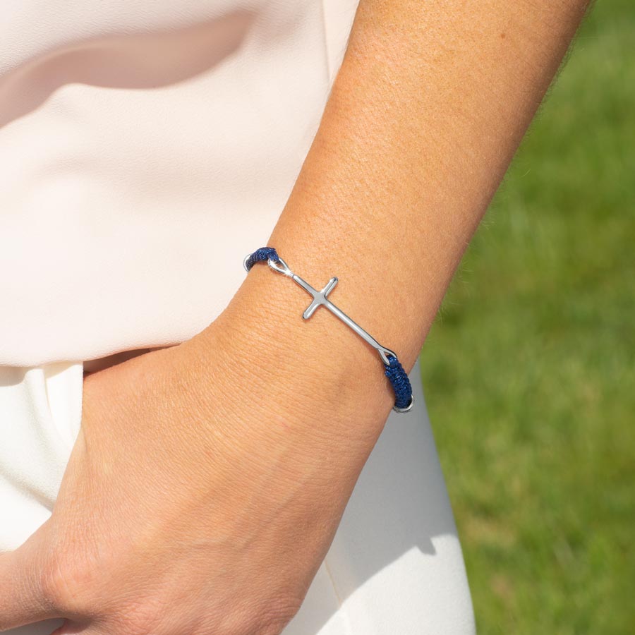 Woman with thumb in pocket wearing navy blue macrame medical ID bracelet with silver cross center piece.