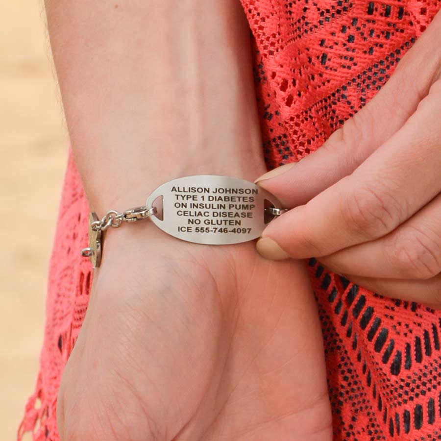 Woman wearing and showing engraving on the Oval Border Medical ID Tag, red caduceus, worn on the Sea Life Medical ID Bracelet