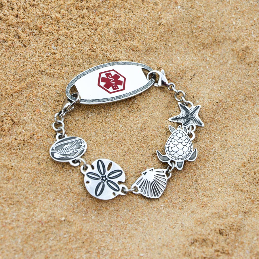 Chain style medical ID bracelet with sea life links including seashell and sand dollar on beach sand