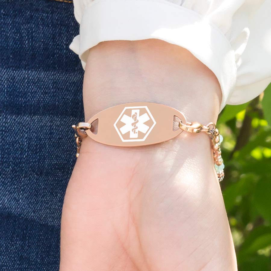 Woman showing decorative rose gold medical ID tag on beaded bracelet