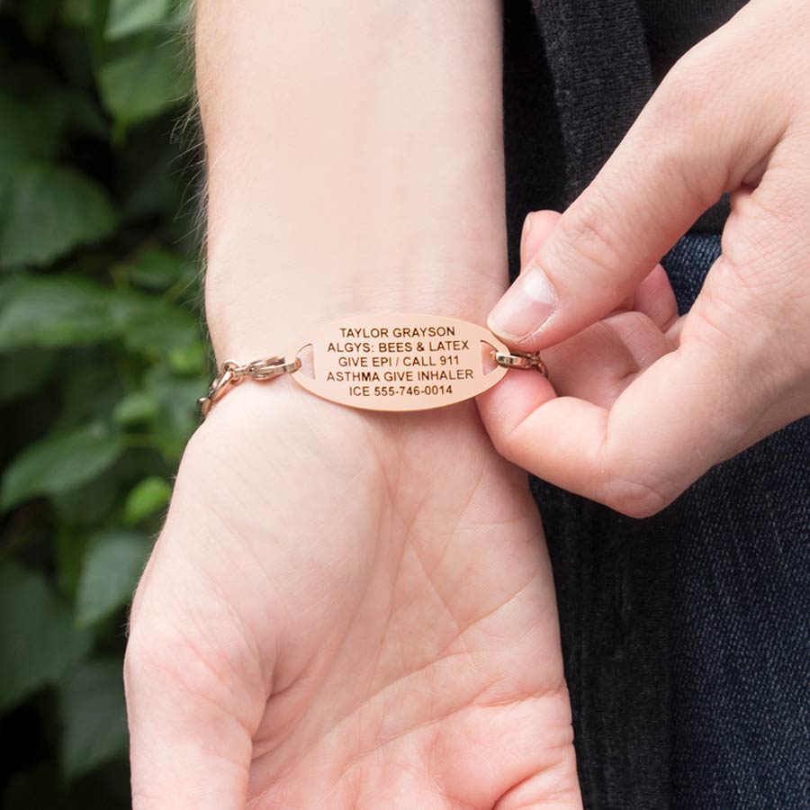 Woman shows engraving on a Rose Gold Tone Oval Med ID Tag on Forever and Always Medical ID with infinity-symbol-shaped links