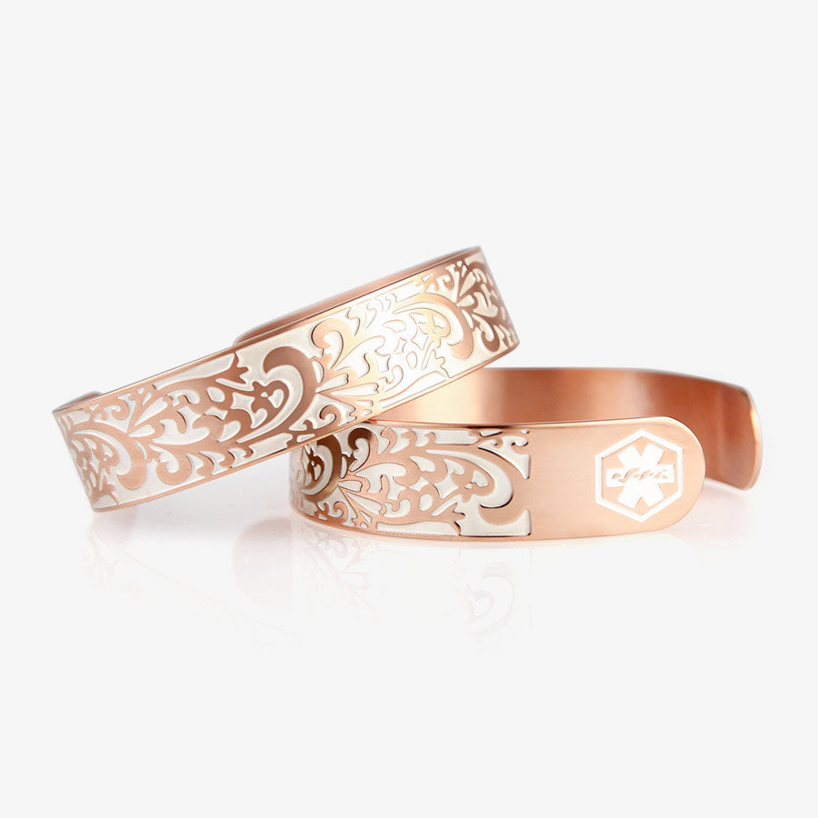 Two identical rose gold tone cuff bracelets with swirl filigree pattern and pearl white medical symbols