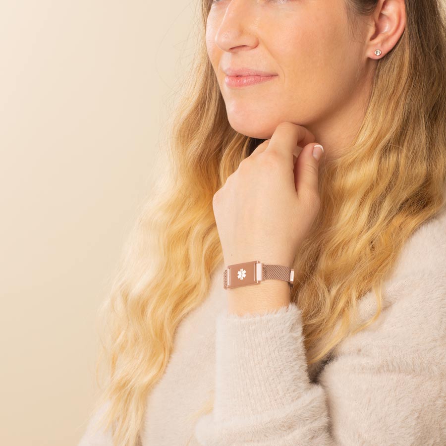 Woman showing the front of Urban Medical Alert in Rose Tone with mesh chain and the affixed medical ID tag with white caduceus