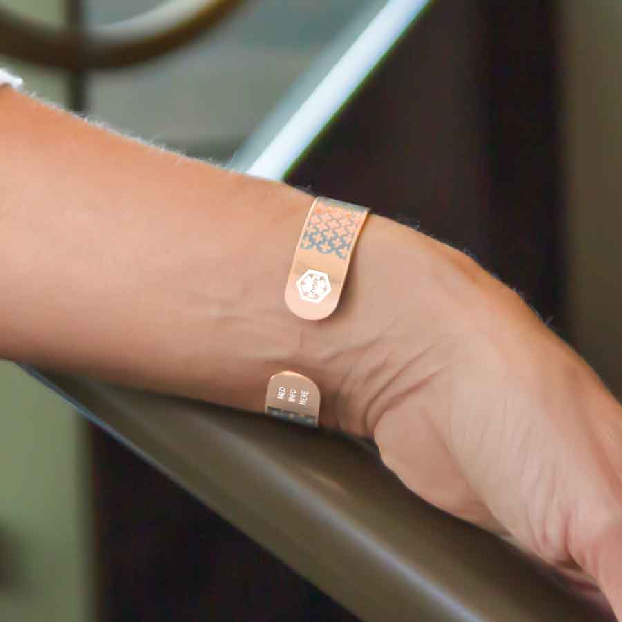 Woman with hand on rail wearing rose gold medical ID cuff bracelet with white medical symbols