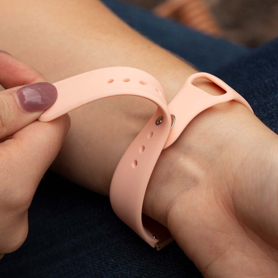 Close-up of pin-tuck watch closure in action on pink silicone band as woman pulls strap back to release bracelet.