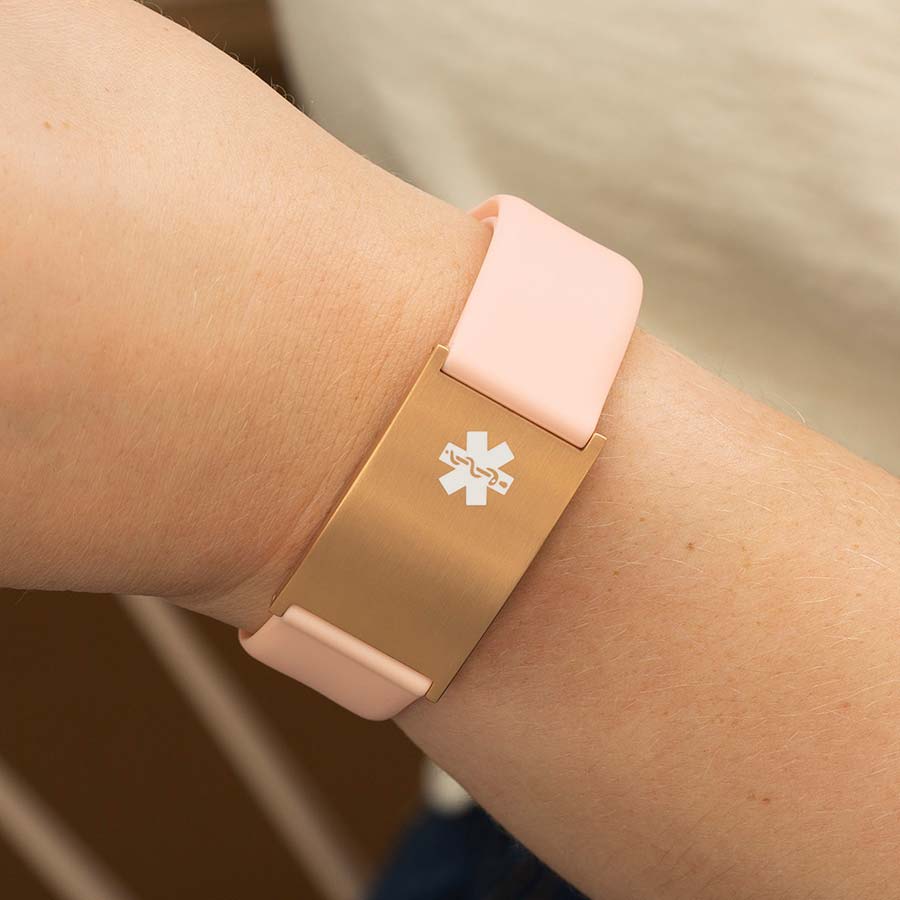 Woman wearing pink silicone medical ID bracelet with oversized Metro ID tag in rose gold.