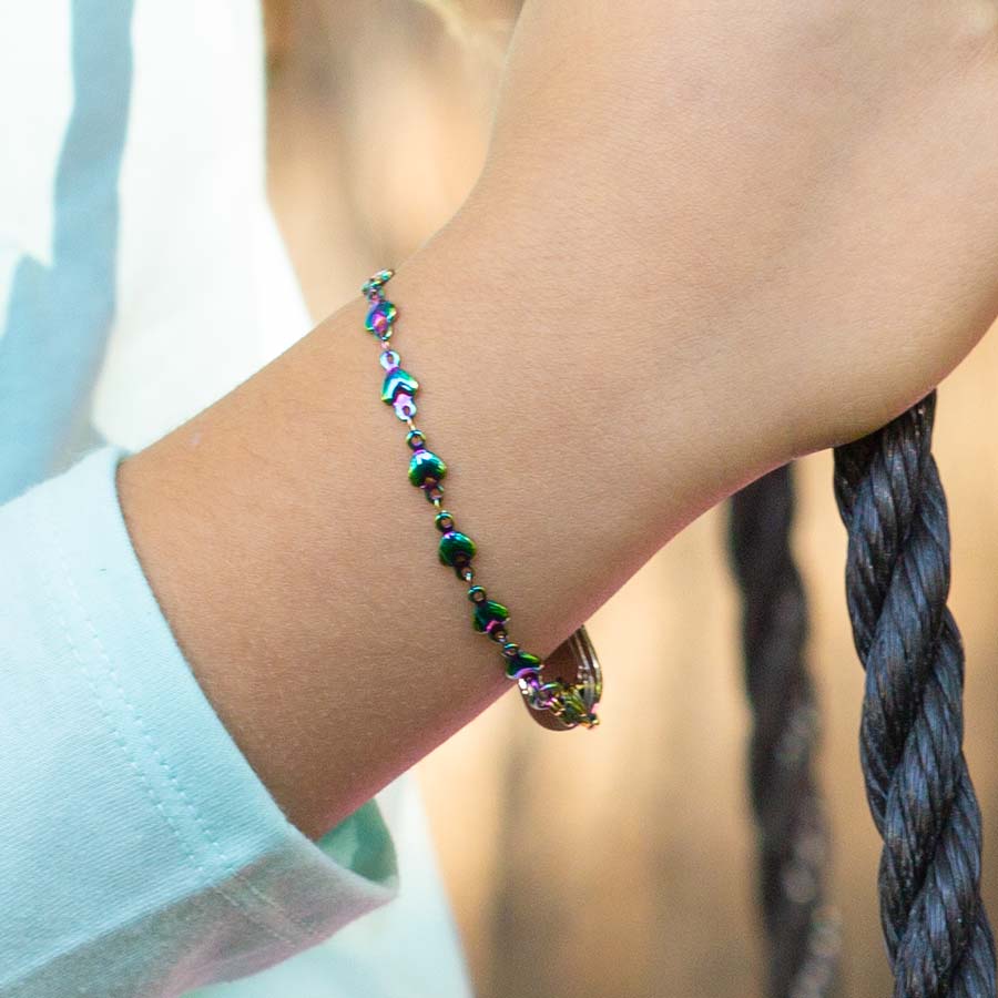 Girl in turquoise top wearing mutli colored magic finish stainless steel heart link chain medical ID bracelet outdoors.