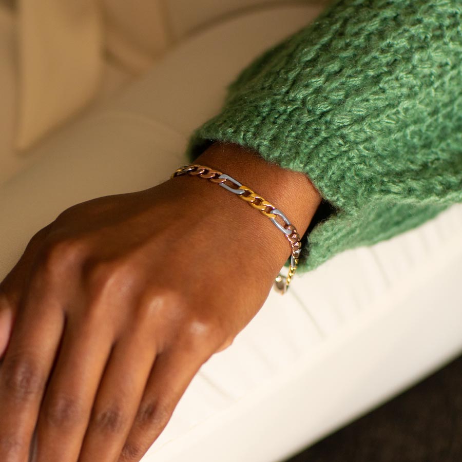 Woman in green sweater and white pants wearing mixed metal stainless steel figaro chain bracelet with silver, rose gold, and gold tones.