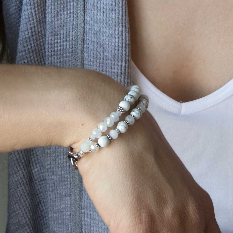 Woman in white top and gray sweater wearing moonstone, crystal, and white jade two strand beaded stretch medical ID bracelet.