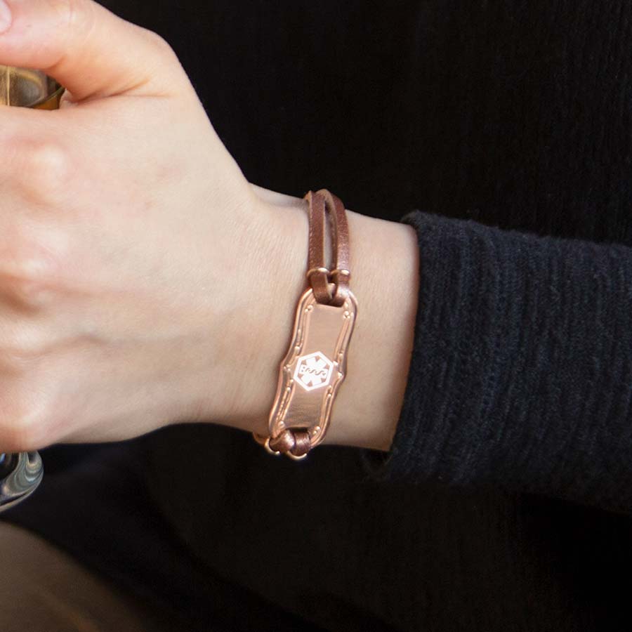 Woman wearing a Medical ID bracelet with a silver tone stainless filigree med ID tag with red caduceus. Only the tag is shown