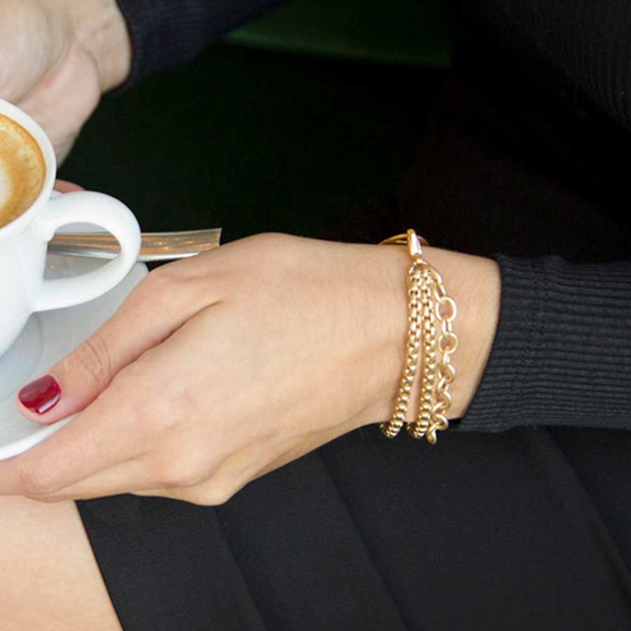 Woman in black top holding mug of coffee wearing three strand gold tone chain medical ID bracelet.