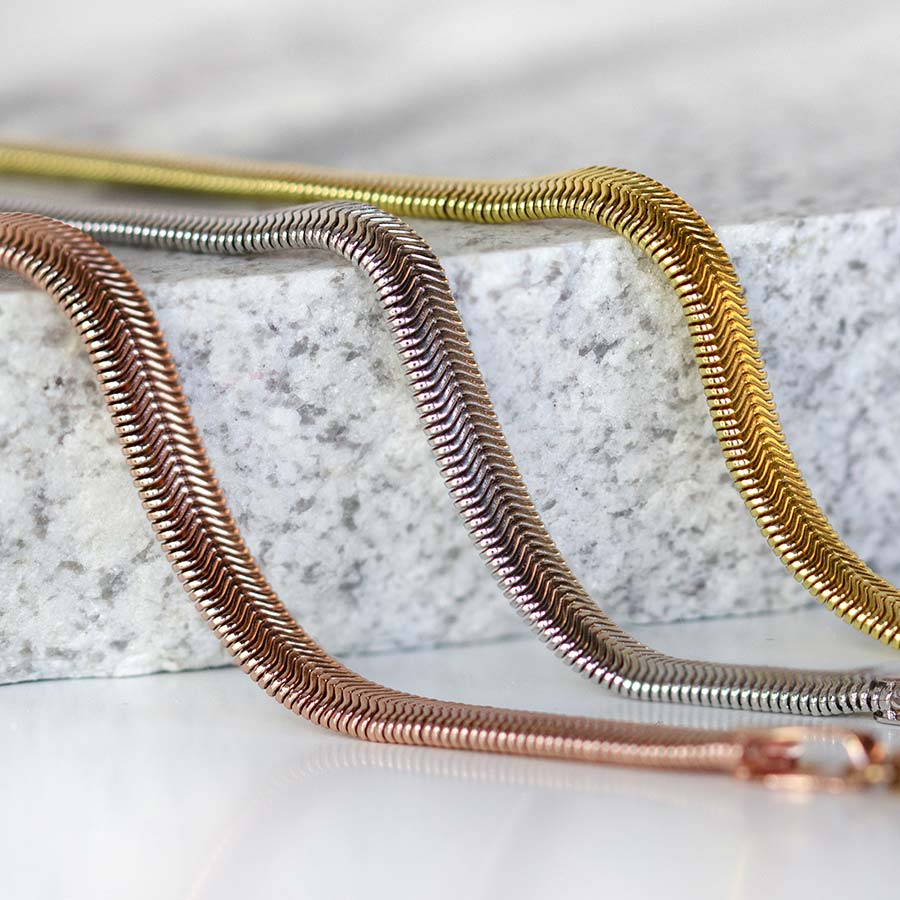 Herringbone medical ID bracelet strands in rose gold, silver, and gold draped over stone slab.