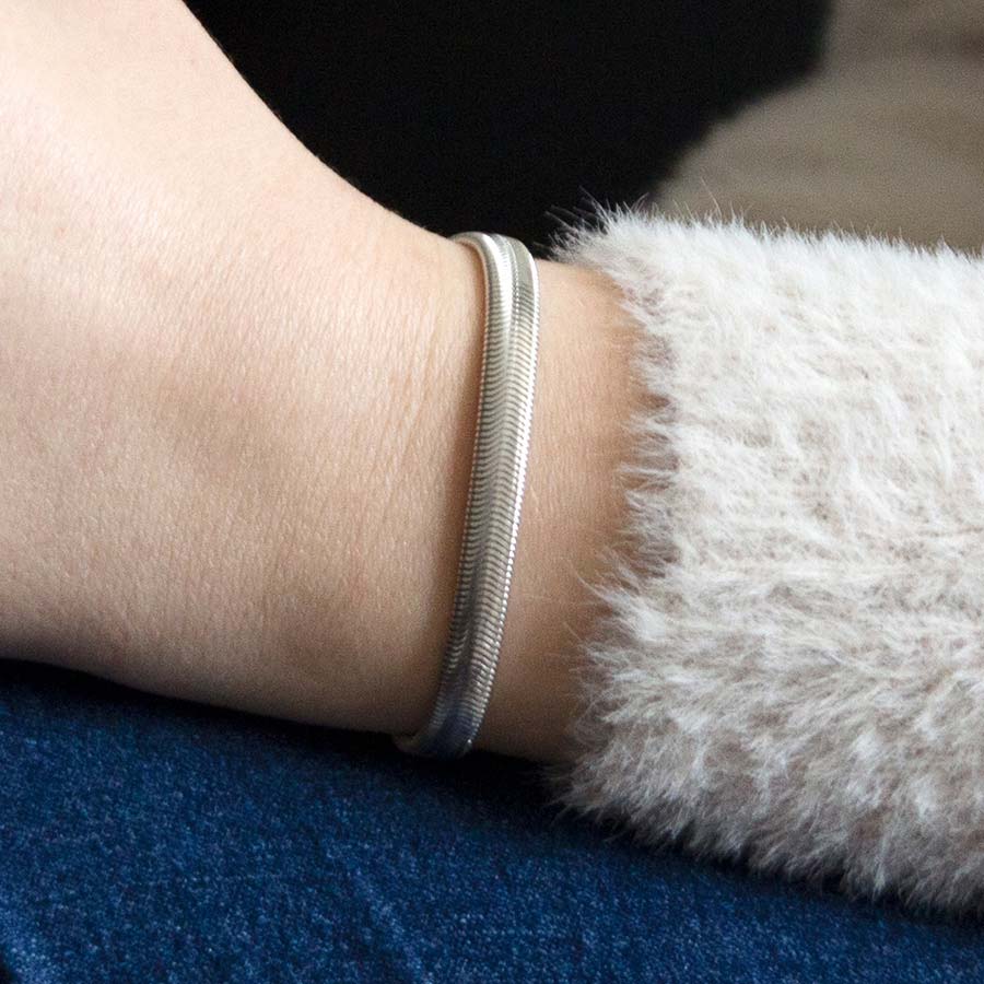 Woman wearing silver herringbone medical ID bracelet showing engraving on back of silver medical ID tag and holding drink.