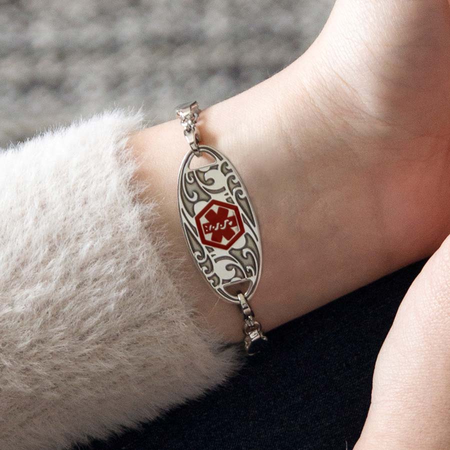 Woman wearing silver herringbone medical ID bracelet with silver filigree design and holding drink.