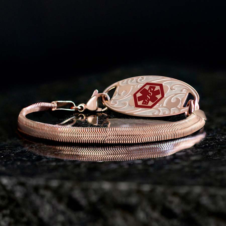 Low angle shot of silver herringbone medical ID bracelet with silver filigree design medical ID tag with red medical caduceus symbol on black stone with text | 2021 COLLECTION LIMITED EDITION.