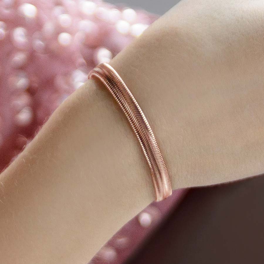 Woman wearing rose gold herringbone medical ID bracelet and holding drink.