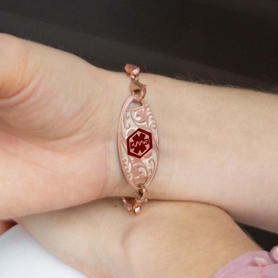 Woman holding drink and wearing rose gold herringbone medical ID bracelet with filigree design medical ID tag overhead shot.