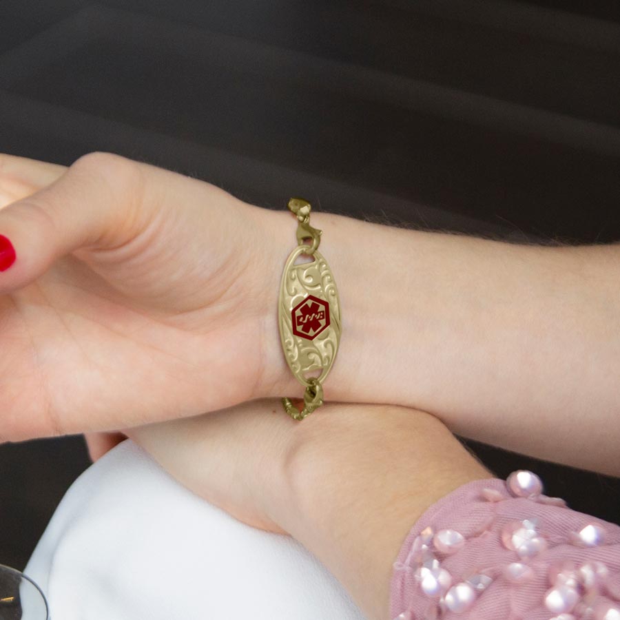 Woman wearing gold herringbone medical ID bracelet with gold filigree design medical ID tag.