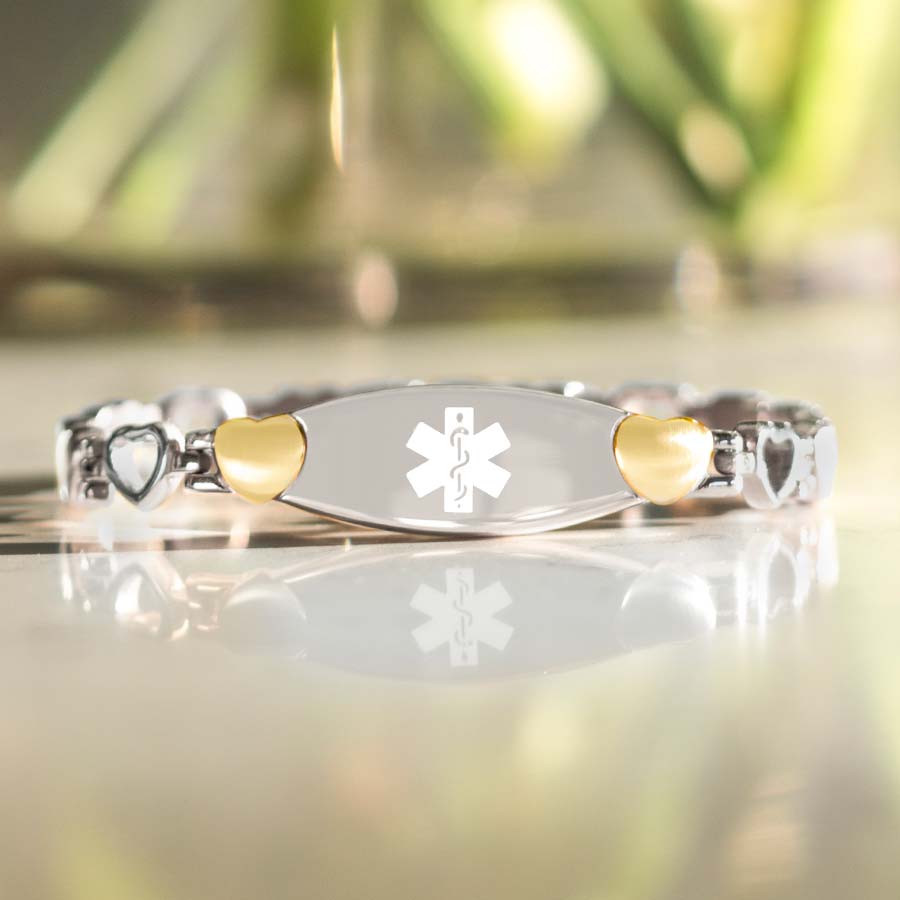 Low angle image of silver and gold linked medical alert bracelet in front of vase of flowers