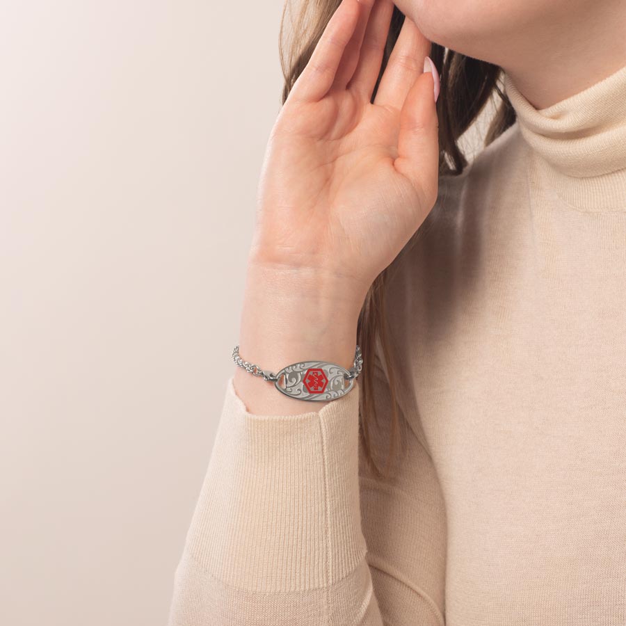 Woman sitting with hand on face wearing silver tone rope chain bracelet and silver medical ID tag with red symbol