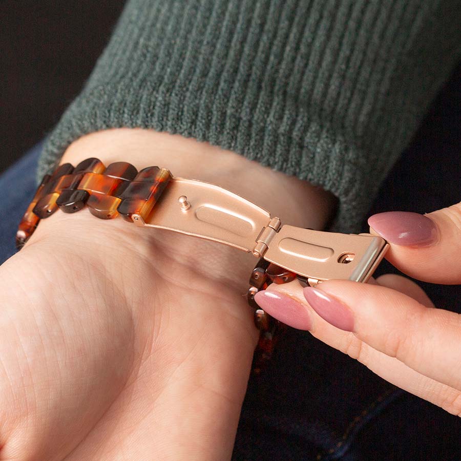 Woman in white sweater holding coffee mug displays tortoiseshell resin and rose gold medical ID bracelet with white caduceus symbol.