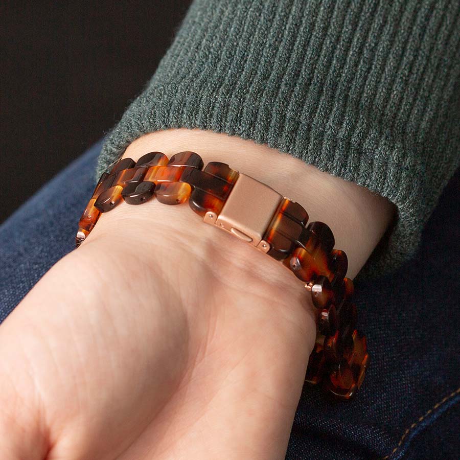 Woman wearing green sweater closing rose gold clasp on medical ID bracelet with tortoiseshell resin band. 